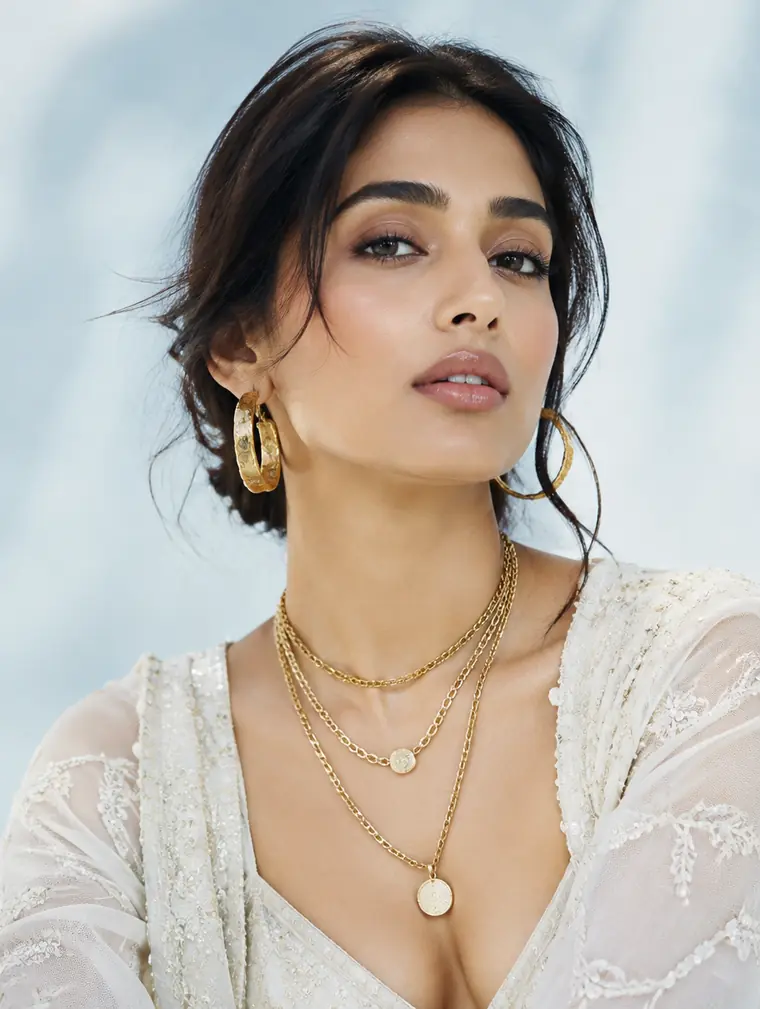 A woman in festive ivory wearing gold hoops and layered gold chains