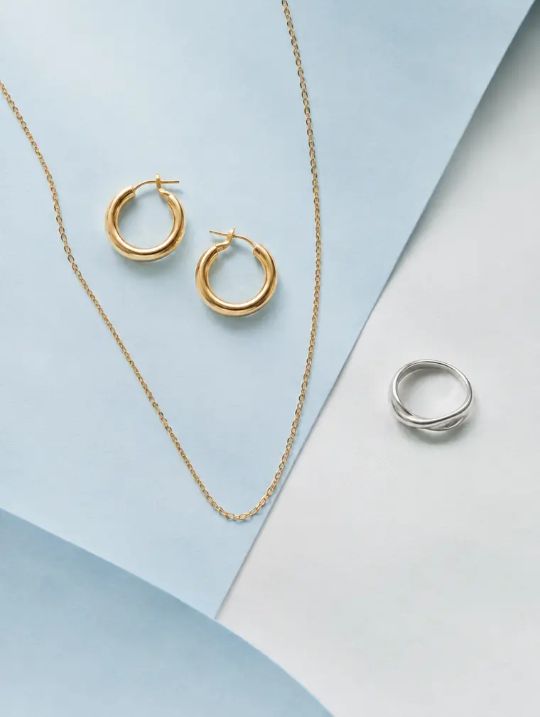 Gold vermeil hoops, a gold chain and a silver ring styled on pale blue paper