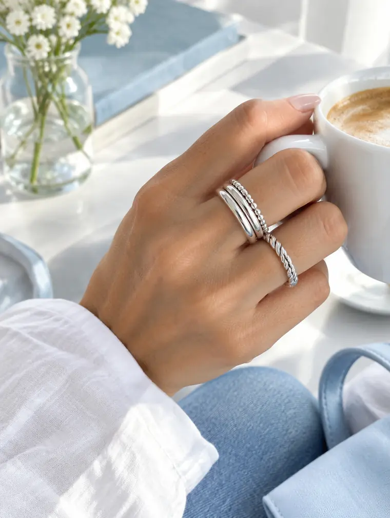 Stacked silver rings on a hand holding a morning coffee